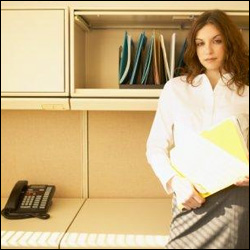 Image of businesswoman in cubicle, sitting on desk next to office phone